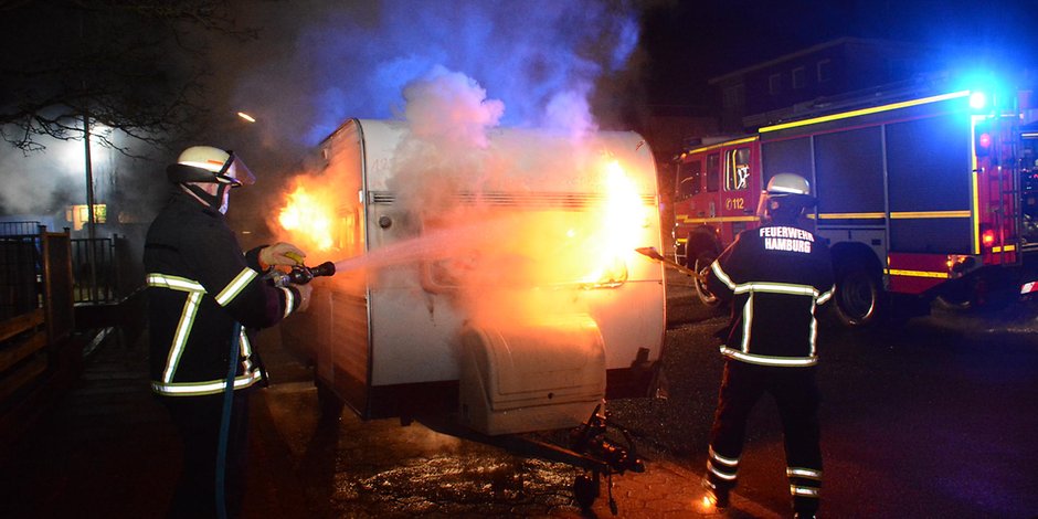 Feuerwehrmänner löschen den brennenden Wohnwagen.