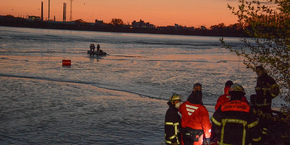 Feuerwehrmänner leiten vom Ufer aus die Rettung ein.