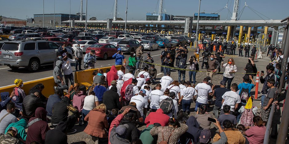 Eine Gruppe Migranten, die T-Shirts mit der Aufschrift „Biden, lass uns bitte rein“ tragen, kniet am Grenzübergang und betet.