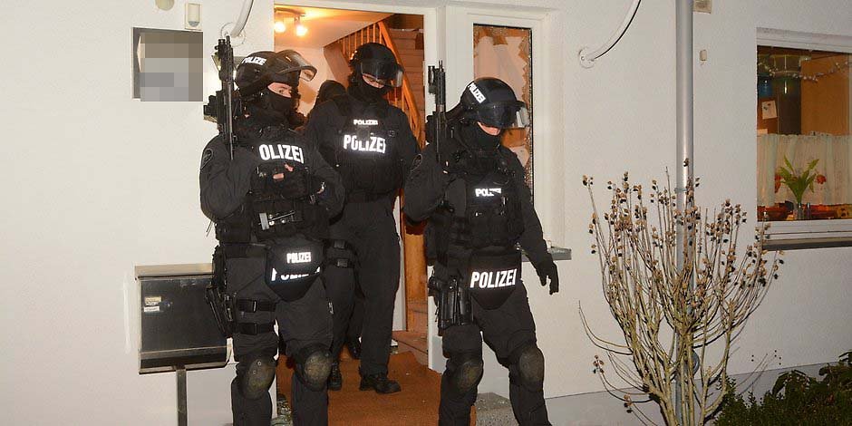 Schwerbewaffnete Männer der Spezialeinheit verlassen das Haus in Farmsen Berne.