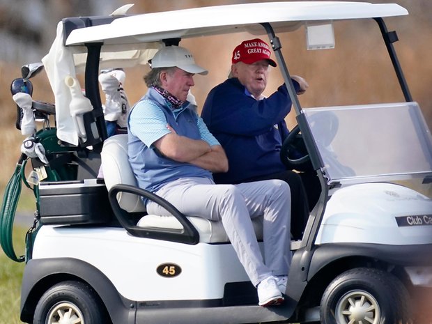 Donald Trump (r.) steuert sein Golfkart über den Golfplatz.