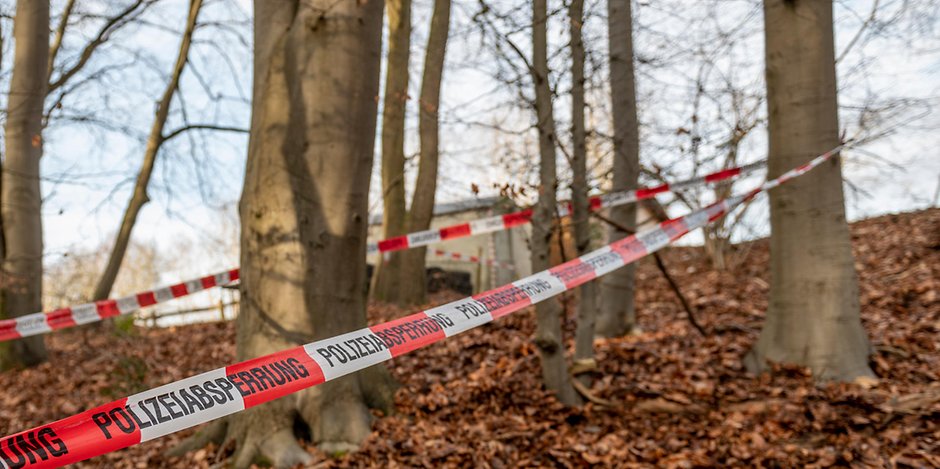 Ein Flatterband der Polizei ist als Absperrung um mehrere Bäume in einem Waldstück bei Seevetal gewickelt.