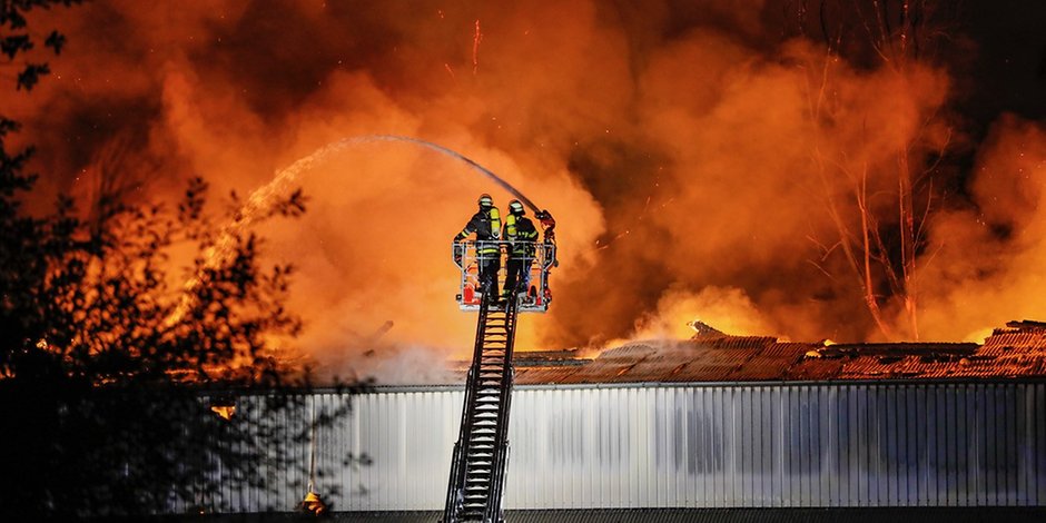 Feuerwehrkräfte bekämpfen die Flammen, die in der Lagerhalle wüten.