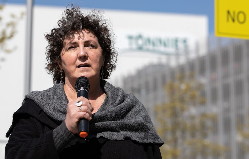 Anja Piel, Mitglied des Deutschen Gewerkschaftsbundes, steht mit einem Mikrofon in der Hand vor dem Betriebsgelände von Tönnies