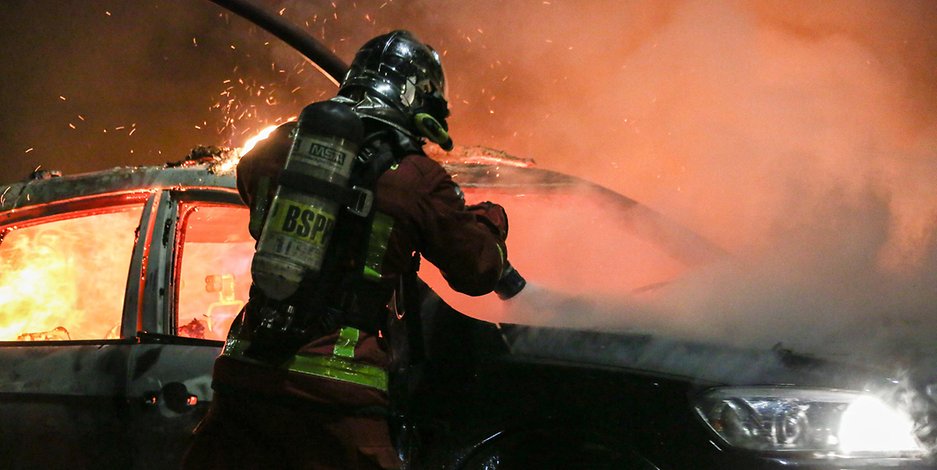 Ein Feuerwehrmann in Frankreich versucht ein brennendes Auto zu löschen (Symbolbild).