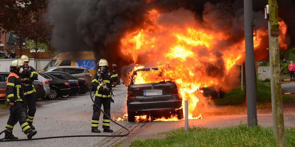 Feuerwehrkräfte stehen am Mercedes, der komplett in Flammen versinkt.