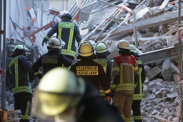 Feuerwehrleute stehen in Düsseldorf vor den Überresten des eingestürzten Gebäudes.