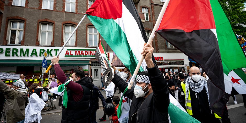 Teilnehmer der Demo verschiedener palästinensischer Gruppen laufen mit Palästina-Flaggen durch Neukölln.