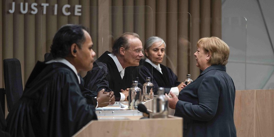 Szene aus dem Film „Ökozid“: Frau Dr. Angela Merkel (Martina Eitner-Acheampong, r), Bundeskanzlerin a.D. im Gespräch mit den Richtern.