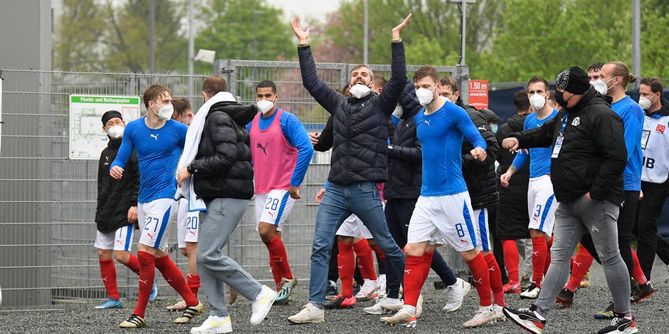 Die Kieler Störche feiern (mit Abstand) den Sieg gegen Regensburg mit ihren Fans vor dem Stadion.