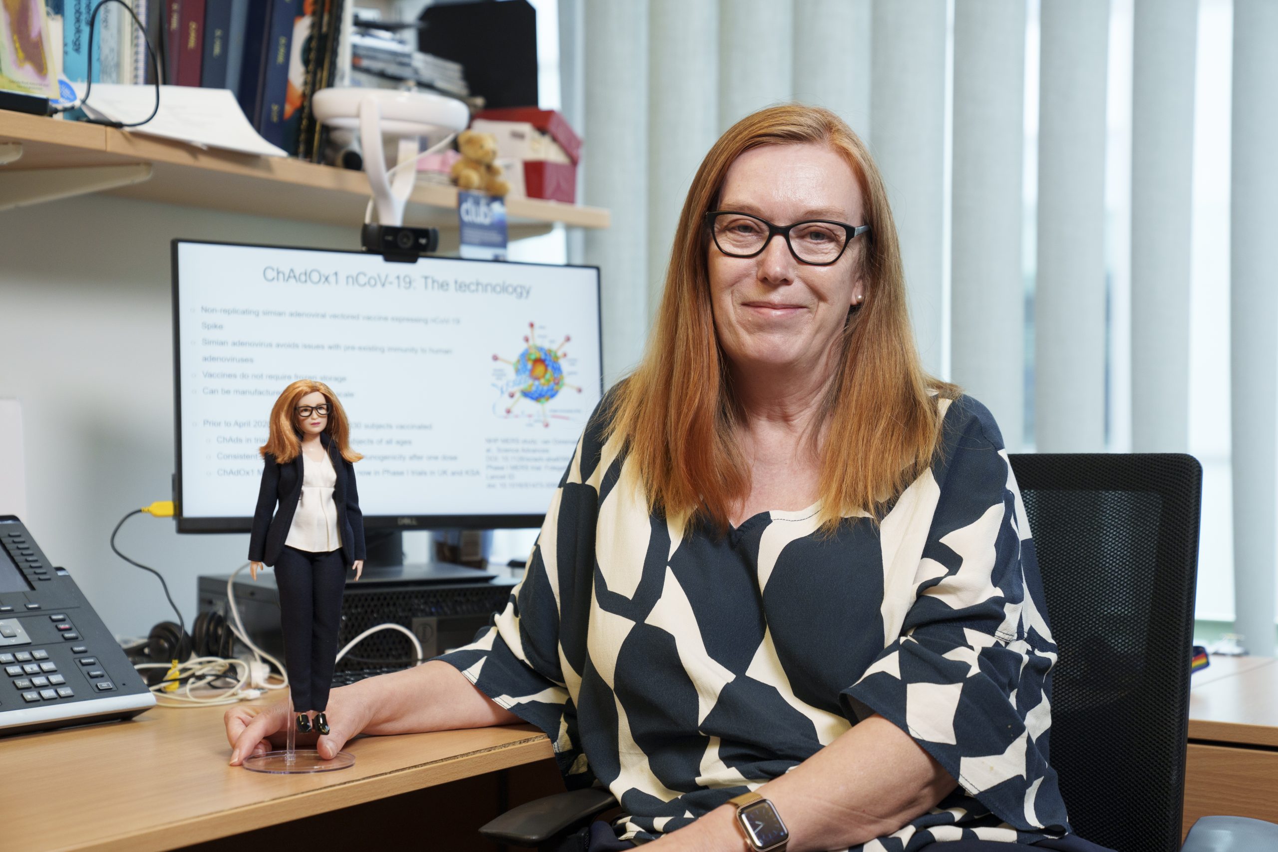 Professorin Dame Sarah Gilbert mit einer ihr zu Ehren hergestellte Barbie-Puppe von Mattel an einem Schreibtisch.