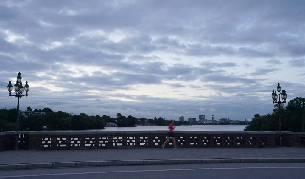 Eine Joggerin läuft im Morgengrauen über die Krugkoppelbrücke an der Außenalster.