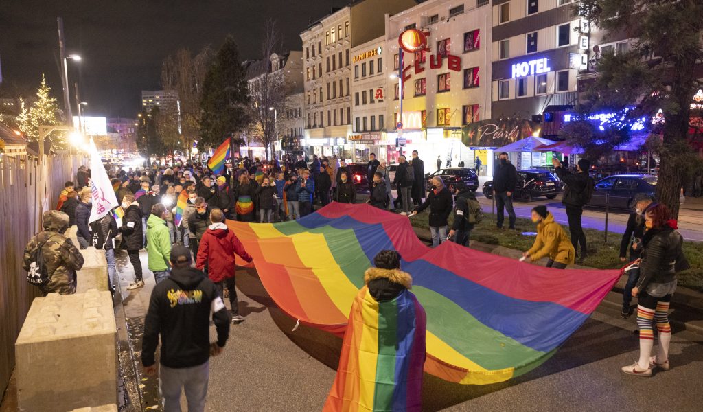 Menschen stehen mit einer großen Regenbogenflagge in der Hand auf einer Demo