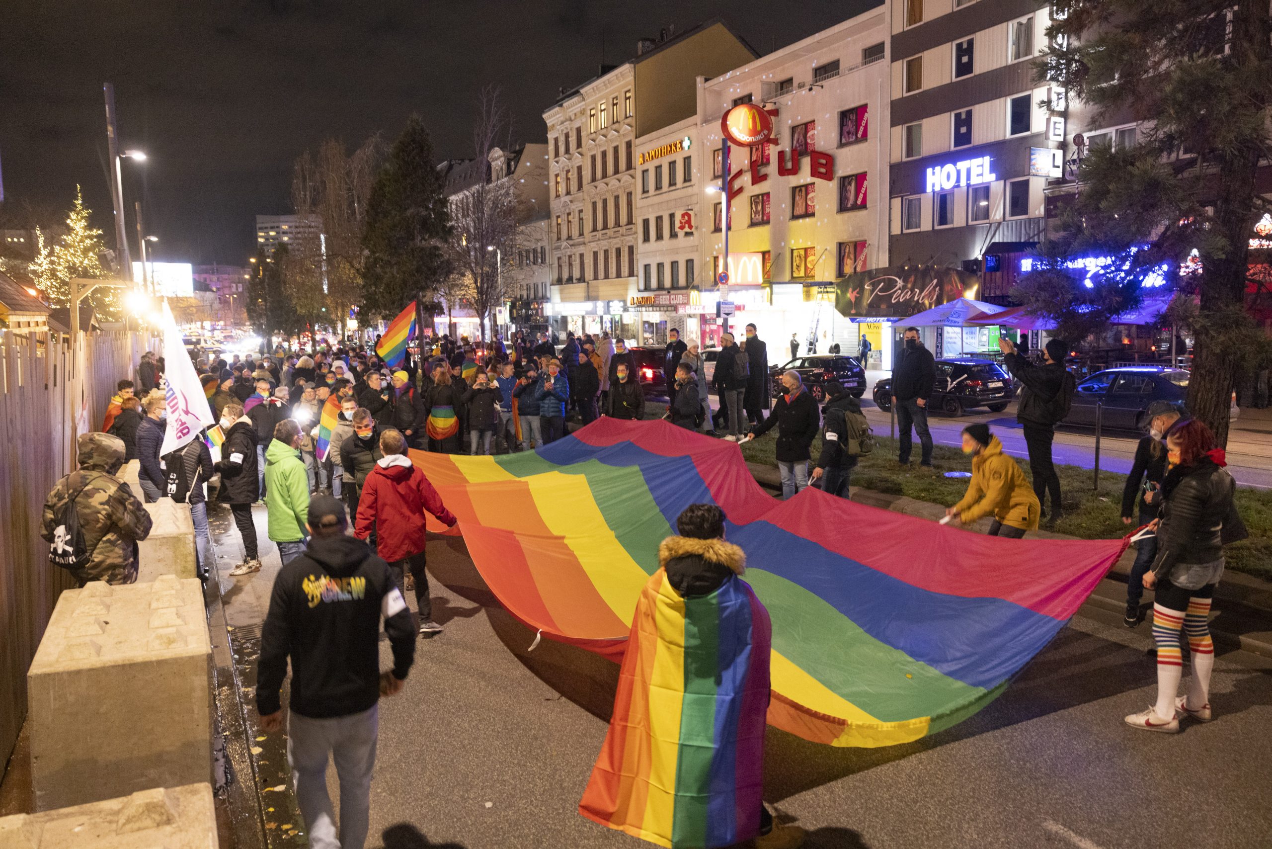 Menschen stehen mit einer großen Regenbogenflagge in der Hand auf einer Demo