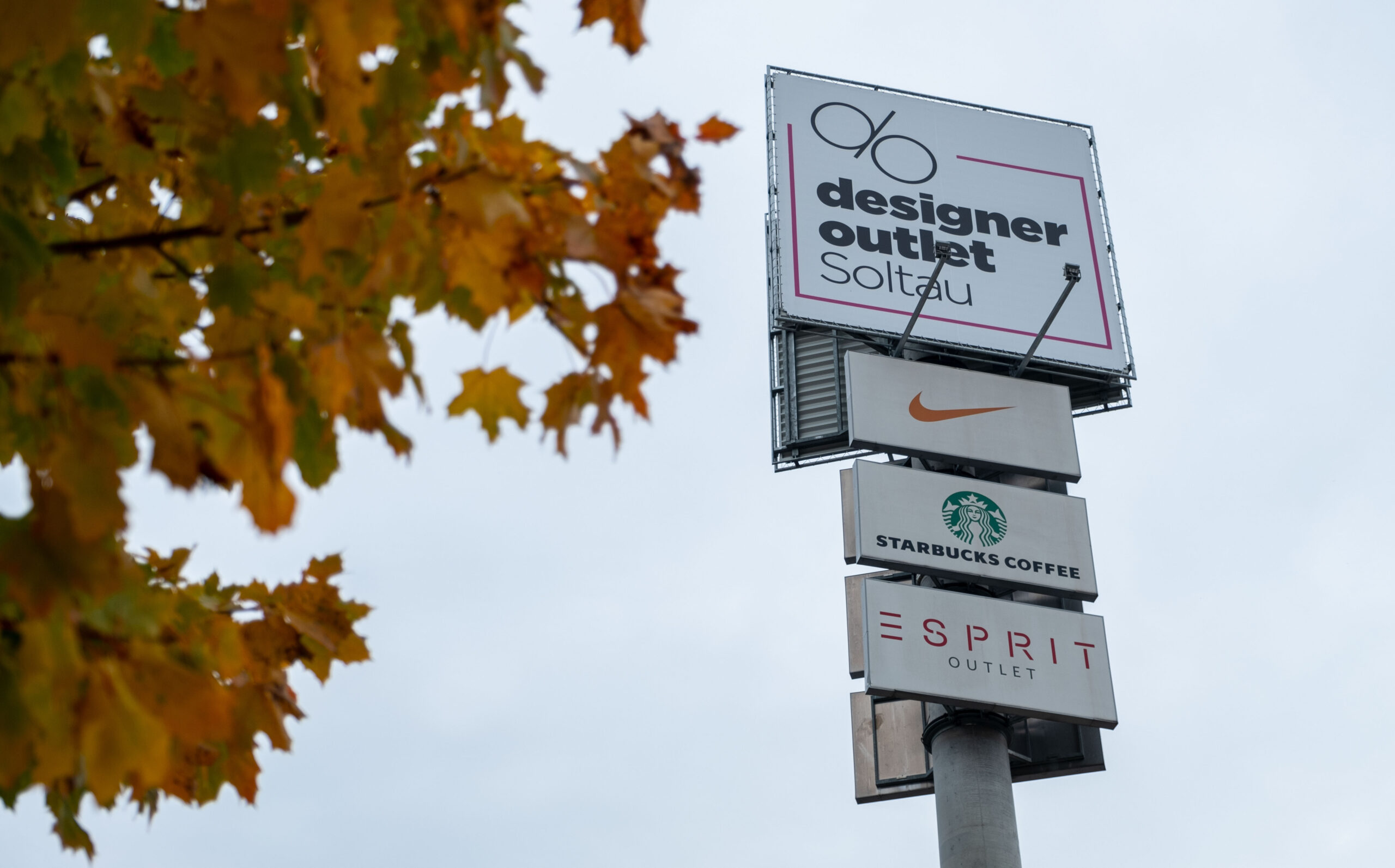 Ein Schild des Designer Outlets. Nike, Starbucks und Esprit-Schilder sind zudem zu sehen.