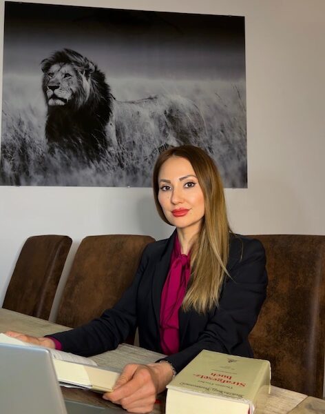 Jacqueline Ahmadi sitzt an einem Tisch vor einem Bild von einem Löwen.