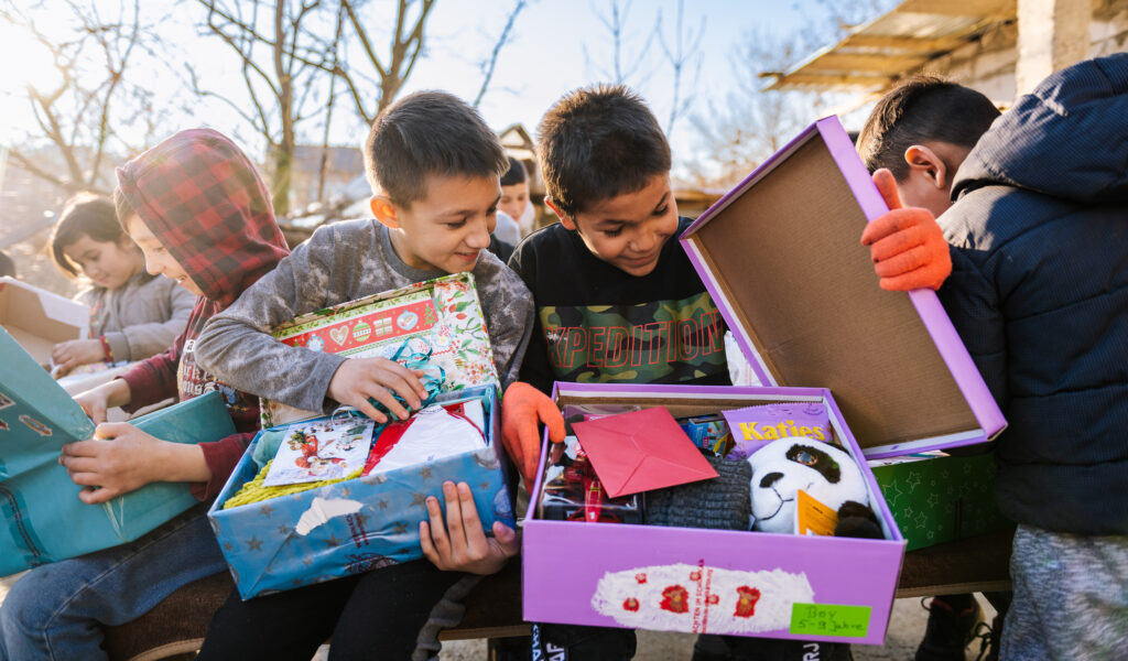 Kinder öffnen lächelnd Schuhkartons mit Geschenken
