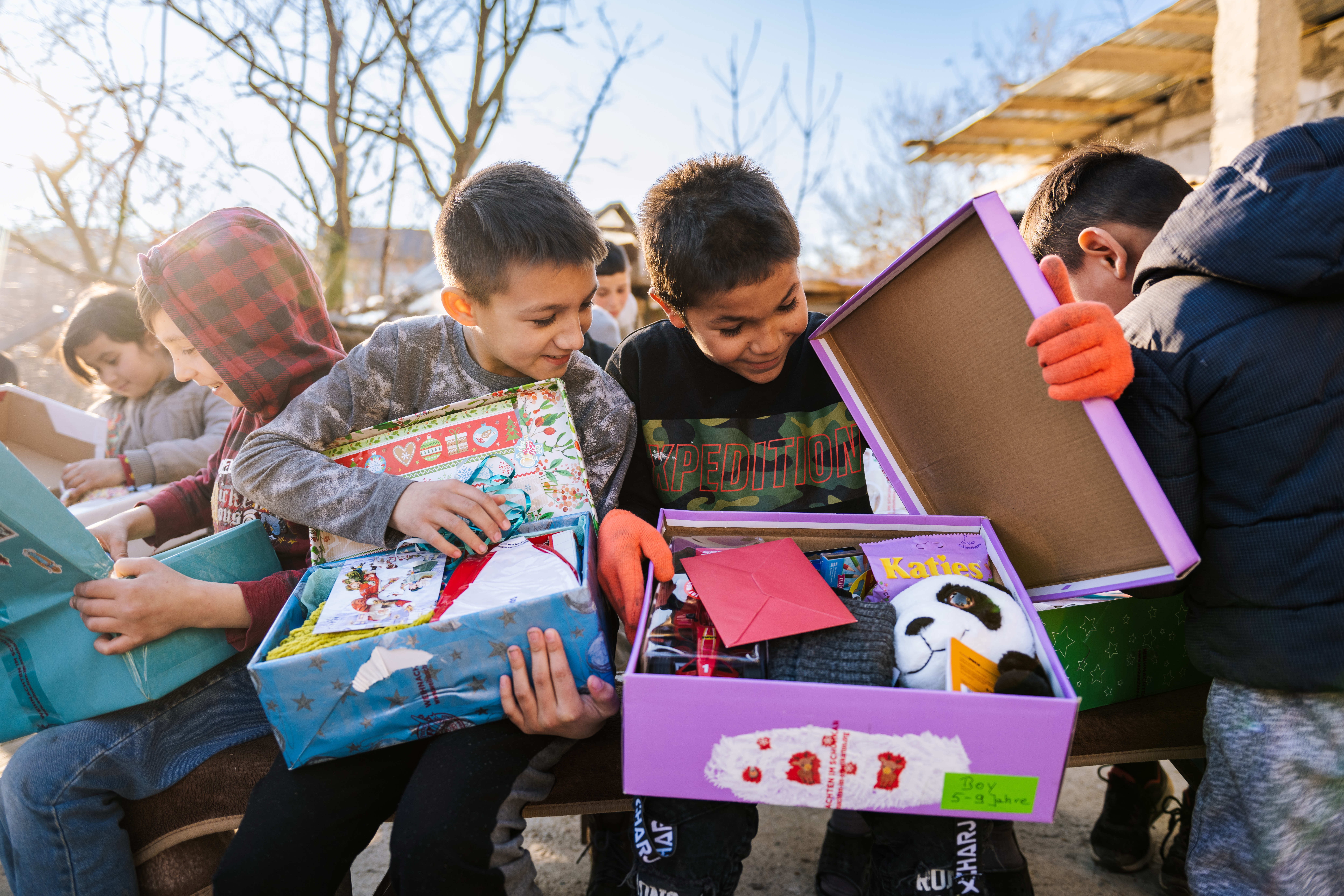 Kinder öffnen lächelnd Schuhkartons mit Geschenken