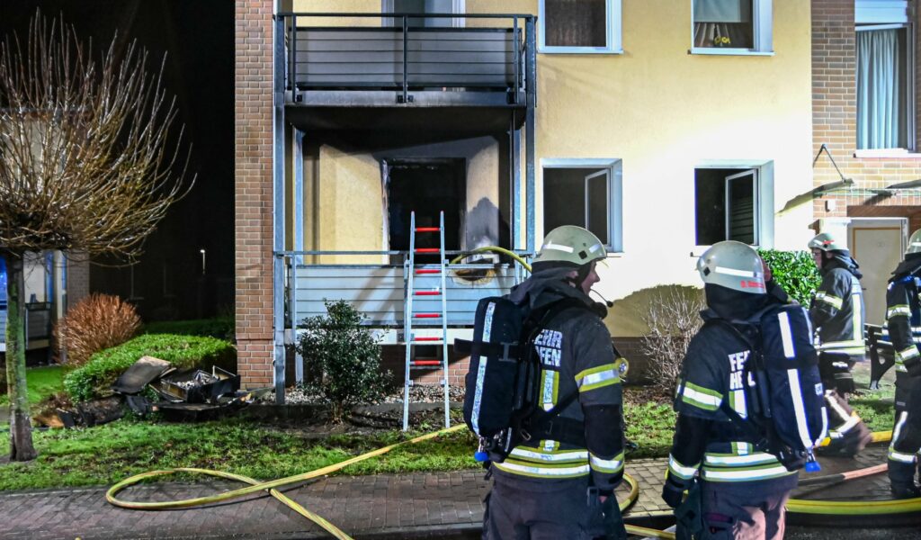Feuerwehrleute stehen vor der ausgebrannten Wohnung