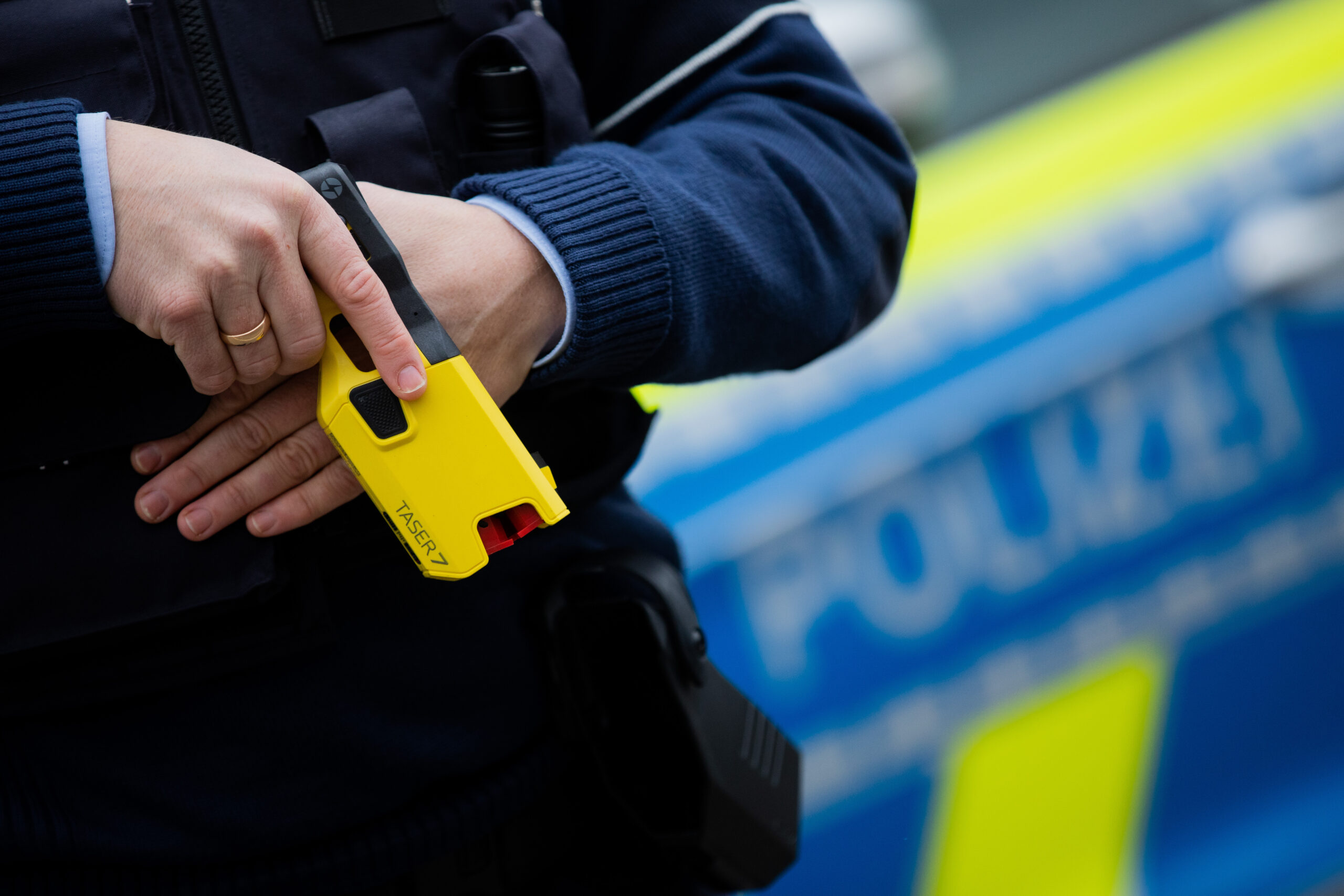 Ein Polizist mit einem Taser in der Hand vor einem Polizeiwagen