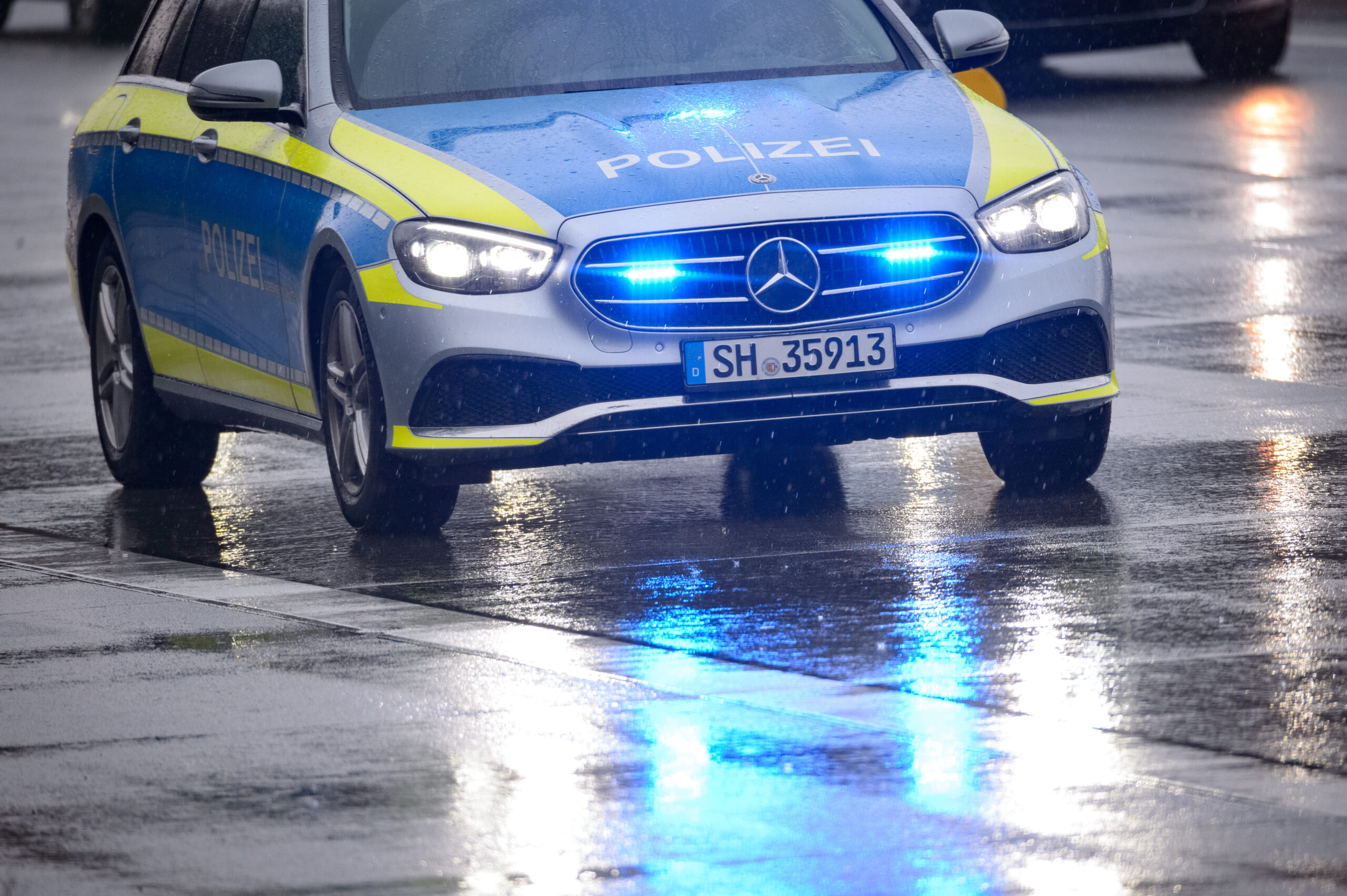 Ein Streifenwagen steht mit Blaulicht auf der regennassen Straße. (Symbolbild)