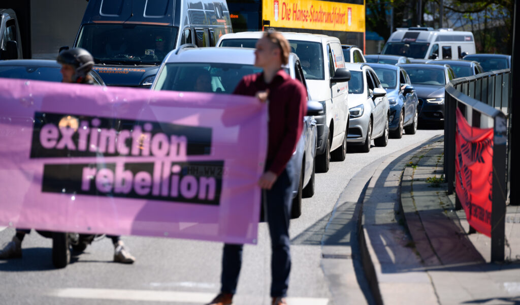 Demonstranten stehen mit einem Plakat mit der Aufschrift „extinction rebellion“ vor wartenden Autos. (Archivbild)