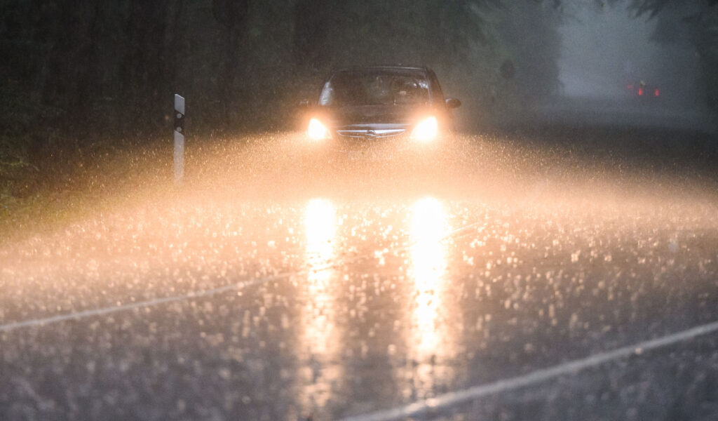 Ein Auto fährt während eines Gewitters mit Starkregen über eine Landstraße