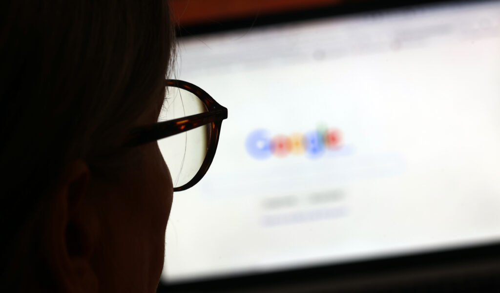 Die Seite der Suchmaschine von Google ist hinter einer Frau mit Brille zu sehen.