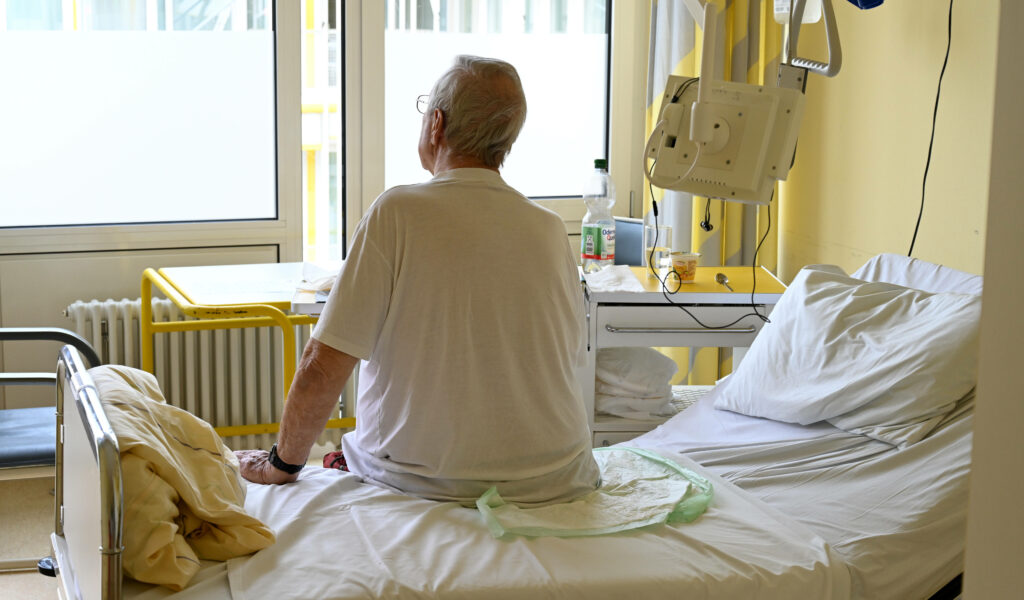 Mann sitzt auf Krankenhausbett