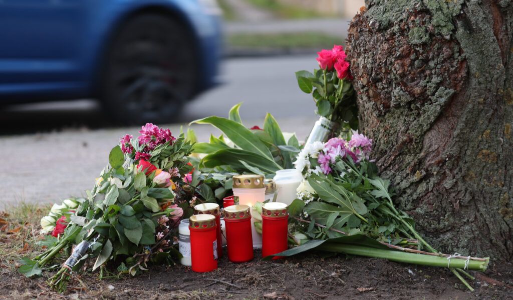 Blumen, Kerzen und Grablichter stehen am Straßenrand an einem Baum, wo am Morgen des 26.12.2022 eine 23-jährige Frau tot gefunden wurde.