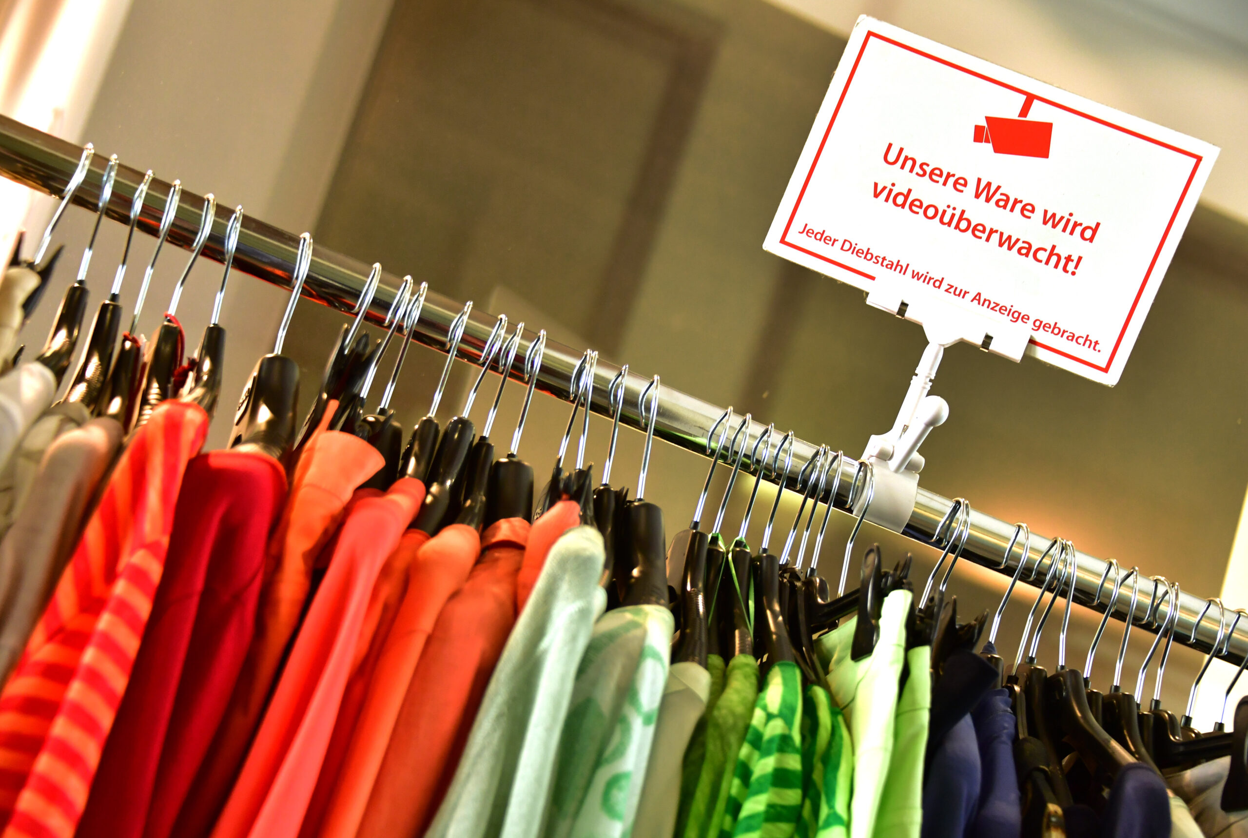 Kleiderstange mit Kleidung in einem Geschäft mit dem Hinweisschild: „Unsere Ware wird videoüberwacht!“