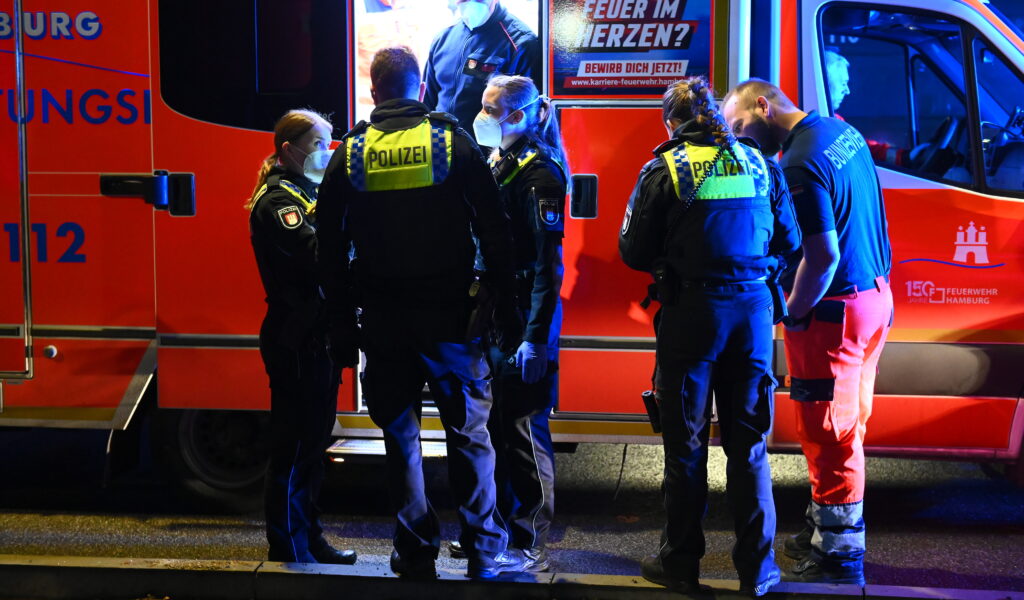 Rettungssanitäter und Polizisten stehen an einem Rettungswagen vor dem Wohnhaus. Bei einem Streit in Hamburg ist dort ein 33-Jähriger mit einem Messer verletzt worden.