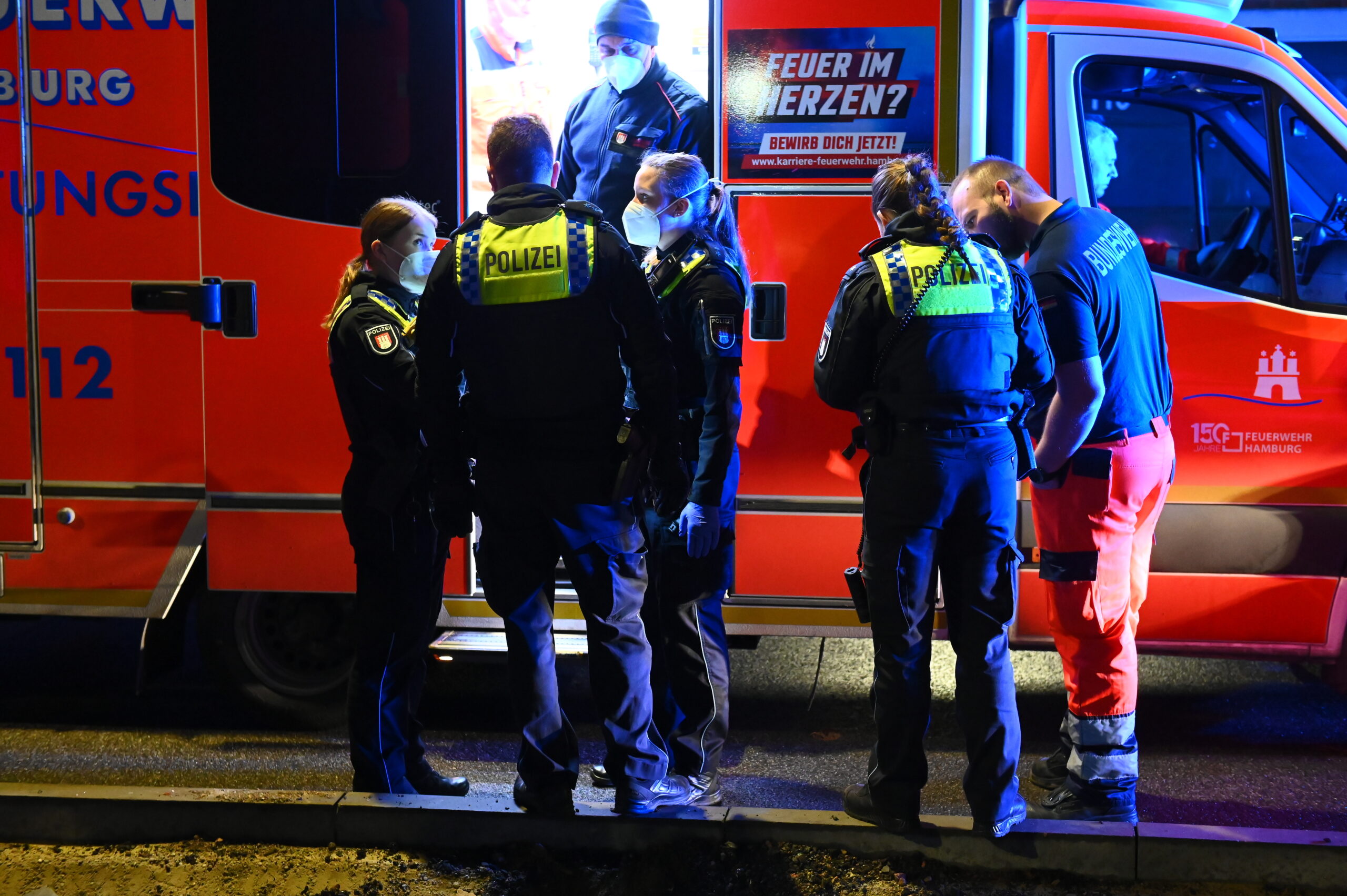 Rettungssanitäter und Polizisten stehen an einem Rettungswagen vor dem Wohnhaus. Bei einem Streit in Hamburg ist dort ein 33-Jähriger mit einem Messer verletzt worden.