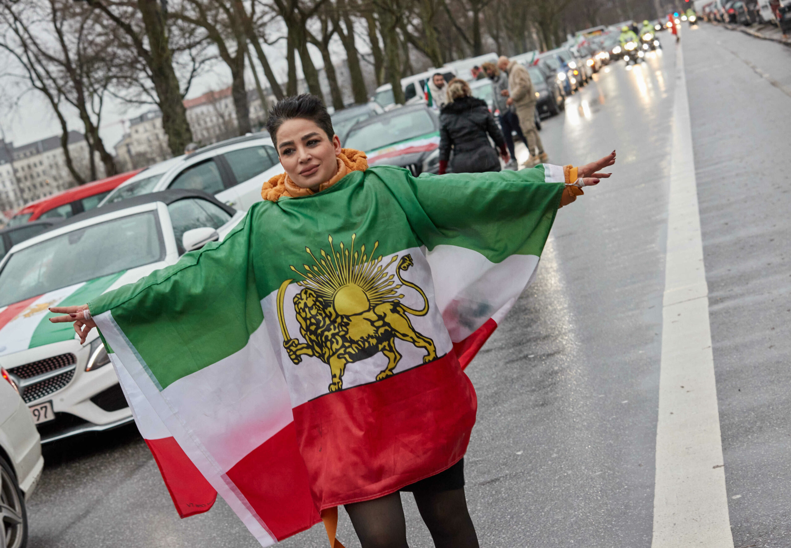 Eine Teilnehmerin der sich zu einem Autokorso als Solidaritätsprotest für den Iran versammelten Demonstranten auf der Glacischaussee trägt eine historische Flagge des Irans.