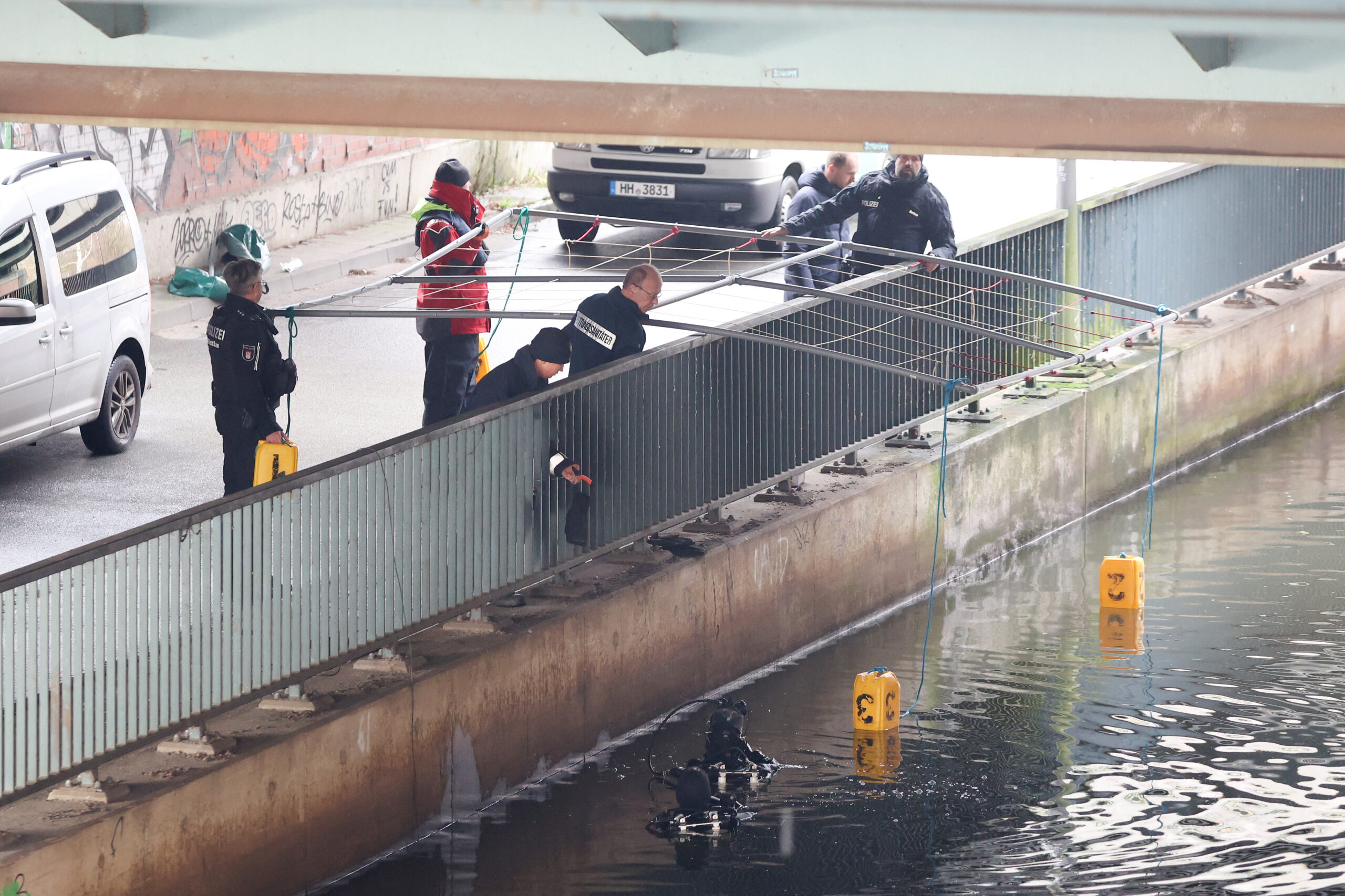 Mit einer Gitterkonstruktion lassen Polizisten in WIlhelmsburg gelbe Bojen zu Wasser. So markieren sie Fundstellen von Körperteilen im Kanal.