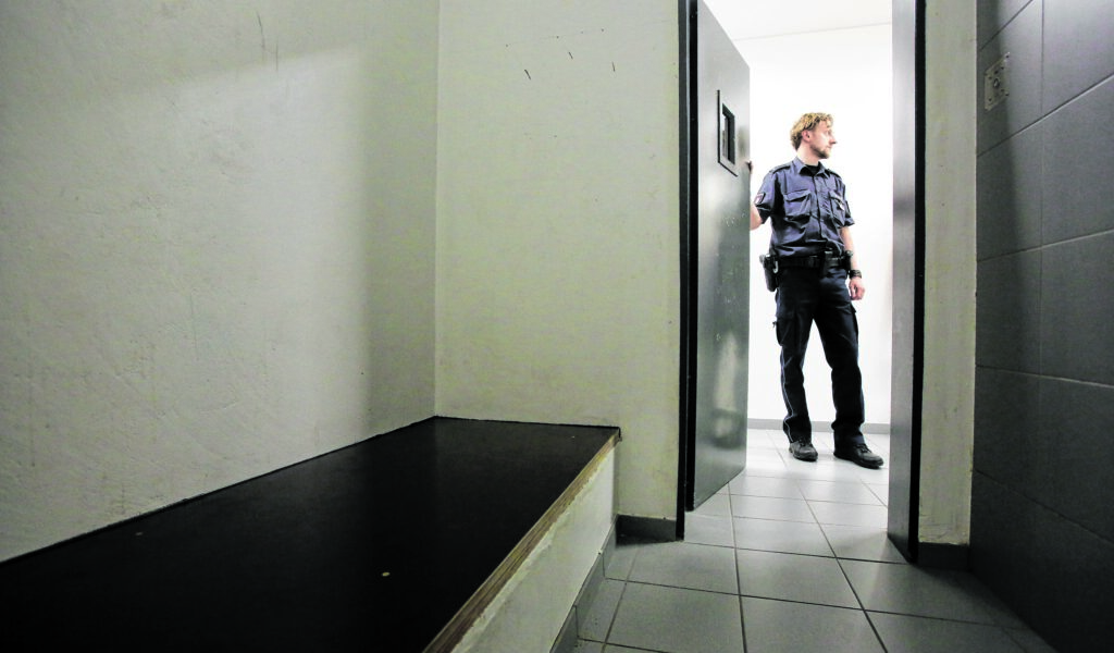Polizist steht an der geöffneten Tür einer Arrestzelle