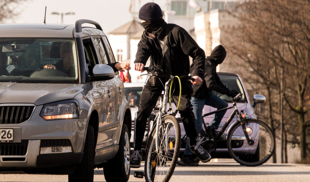 Teilnehmer eines Autokorsos gegen Corona-Maßnahmen fahren durch die Innenstadt, während Gegendemonstranten auf Fahrrädern die Fahrt stören